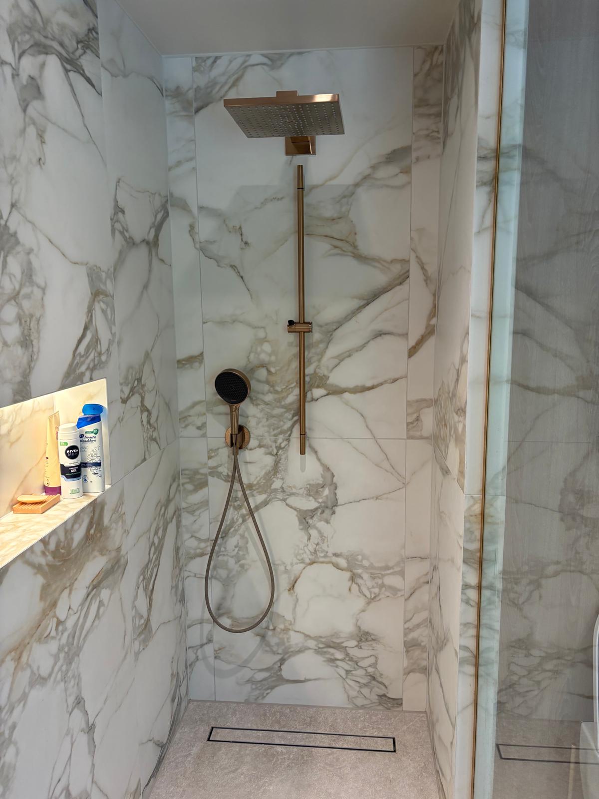 Shower with square brass rainhead against book-matched marble walls