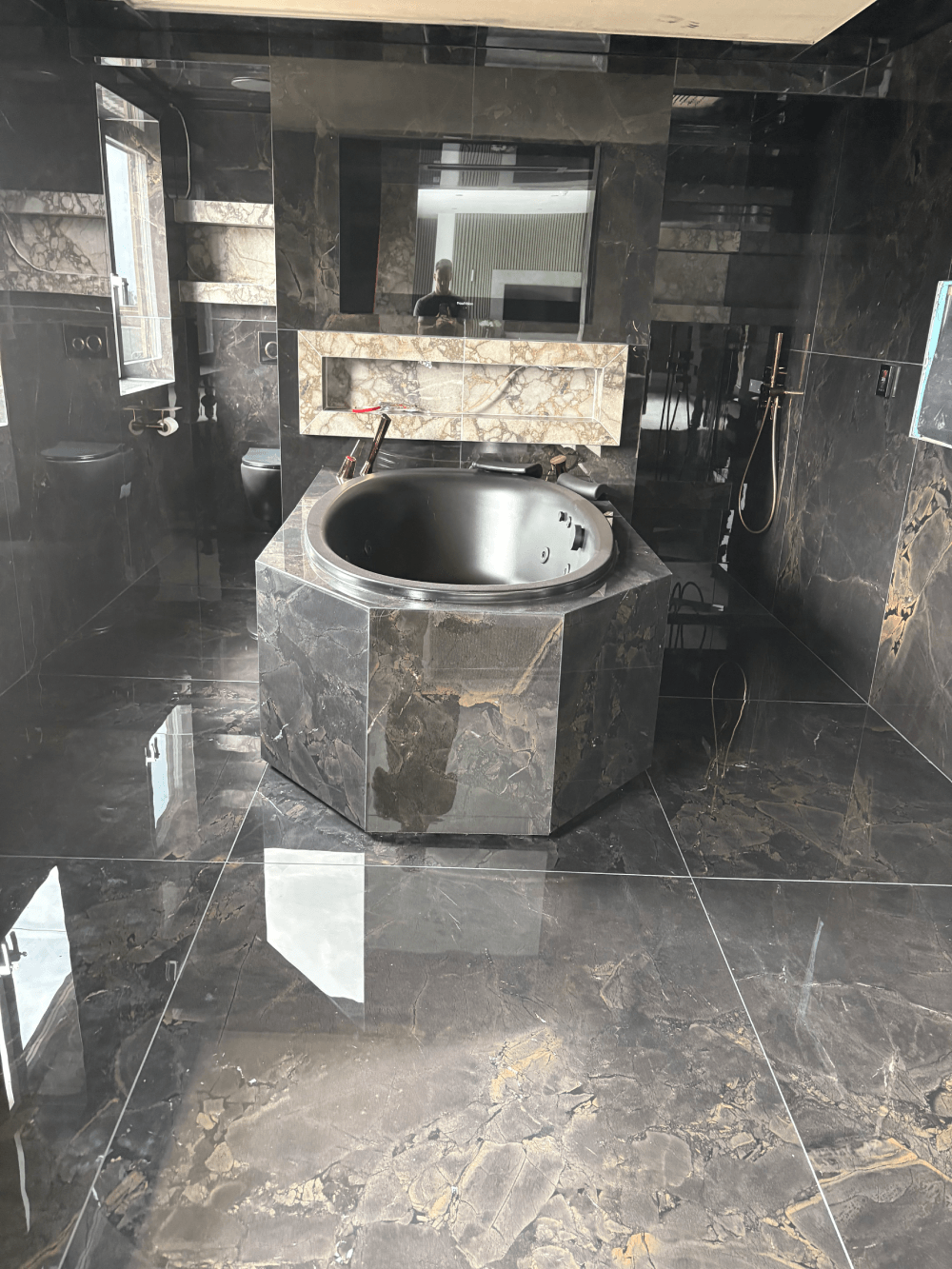 Hexagonal stone-clad bath surround within a fully tiled bathroom